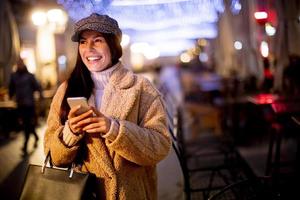 Jolie jeune femme utilisant son téléphone portable dans la rue au moment de Noël