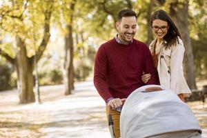 heureux jeunes parents marchant dans le parc et conduisant un bébé dans une poussette