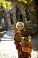 Senior woman walking avec panier plein de fleurs et d'épicerie en automne park photo