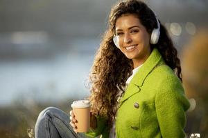 jolie jeune femme écoutant de la musique avec un smartphone et du café à emporter au bord de la rivière par une journée ensoleillée d'automne photo