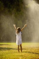 jolie petite fille s'amusant sous un arroseur d'irrigation photo