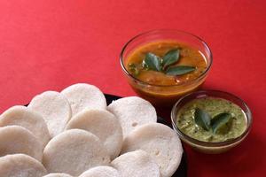 idli avec sambar et chutney de noix de coco sur fond rouge, plat indien plat préféré de l'Inde du Sud rava idli ou semoule oisivement ou rava oisivement, servi avec du sambar et du chutney vert. photo