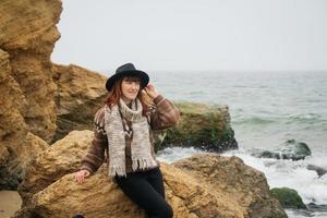 femme dans un chapeau et une écharpe debout sur un rocher contre une belle mer à l'horizon