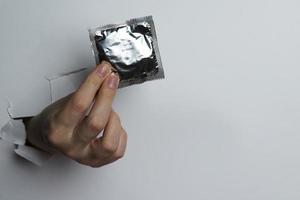 main féminine tenant un préservatif, sur fond blanc. photo