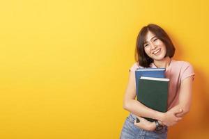 belle femme asiatique étudiant universitaire heureux sur fond jaune photo