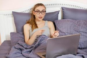 jolie femme adolescente utilisant son ordinateur portable au lit. belle fille à lunettes travaillant sur ordinateur portable dans la chambre photo