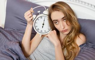 jeune belle fille endormie tenant une horloge et se trouve dans son lit dans la chambre le matin. photo