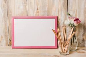 cadre blanc vierge avec bordure rose crayons de couleur verre bureau en bois