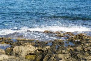 les vagues se brisant sur une plage de galets, formant un embrun. vague et éclaboussures sur la plage. les vagues se brisent sur les rochers. photo