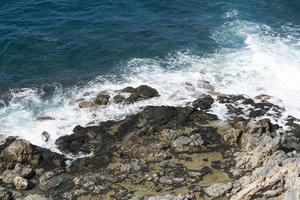 les vagues se brisant sur une plage de galets, formant un embrun. vague et éclaboussures sur la plage. les vagues se brisent sur les rochers. photo