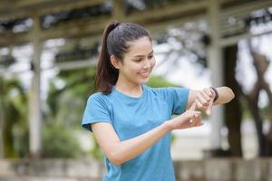heureuse jeune femme en vêtements de sport à l'aide d'une montre intelligente tout en faisant de l'exercice dans le parc