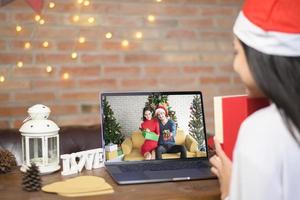 jeune femme souriante portant un chapeau de père noël rouge faisant un appel vidéo sur le réseau social avec la famille et les amis le jour de noël. photo