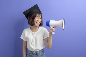 Portrait d'un étudiant asiatique diplômé tenant un mégaphone isolé sur fond violet studio photo