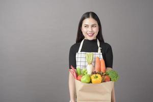 Portrait de belle jeune femme avec des légumes dans un sac d'épicerie en studio fond gris photo