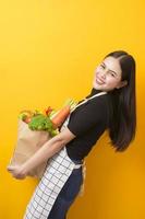 belle jeune femme tient des légumes dans un sac d'épicerie en studio fond jaune photo