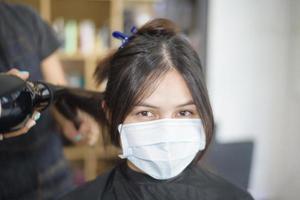 une jeune femme se fait couper les cheveux dans un salon de coiffure, portant un masque facial pour la protection covid-19, concept de sécurité du salon photo