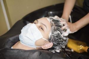 une jeune femme se fait couper les cheveux dans un salon de coiffure, portant un masque facial pour la protection covid-19, concept de sécurité du salon photo