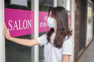 une jeune femme porte un masque facial pour la protection covid-19 debout devant le magasin du salon, concept de sécurité du salon photo