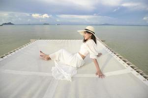 une belle femme heureuse en robe blanche s'amusant et se relaxant sur la terrasse de l'île tropicale et l'océan clair turquoise, le concept d'été et de vacances photo