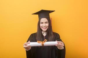 portrait d'une belle femme heureuse en robe de graduation tient un certificat d'études sur fond jaune photo