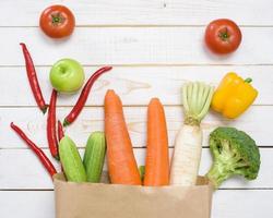 légumes dans un sac d'épicerie sur fond de bois blanc photo