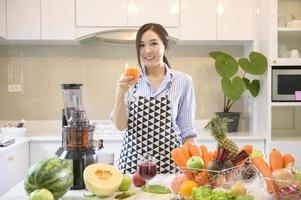 une belle femme prépare des jus de fruits frais et sains, tandis que des légumes et des presse-agrumes sur la table dans la cuisine, concept de santé photo