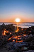 feu de joie avec du bois de chauffage brûlant pendant le beau coucher de soleil à la plage