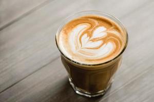 gros plan de café fraîchement moulu dans un verre tumbler avec un bel art latte sur fond de table en bois photo