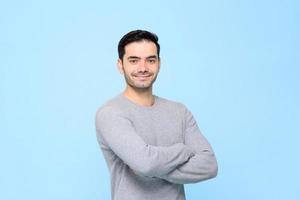 Portrait d'un bel homme souriant et sympathique en t-shirt gris uni avec les bras croisés isolé dans un studio bleu clair bakground photo