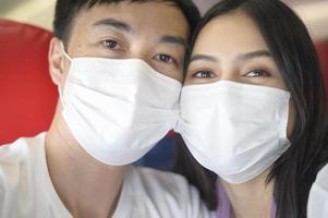 un jeune couple de voyageurs prenant un sefie porte un masque de protection à bord de l'avion, voyage sous la pandémie de covid-19, voyages de sécurité, protocole de distanciation sociale, nouveau concept de voyage normal photo