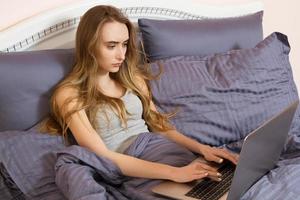 jolie femme adolescente utilisant son ordinateur portable au lit. belle fille à lunettes travaillant sur ordinateur portable dans la chambre photo
