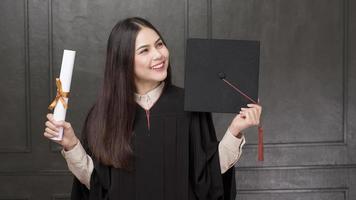 Portrait de jeune femme en robe de graduation souriant et acclamant sur fond noir photo