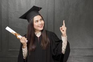 Portrait de jeune femme en robe de graduation souriant et acclamant sur fond noir photo