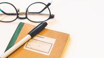 cahier de couverture en papier artisanal marron avec stylo et lunettes sur fond blanc isolé de bureau.