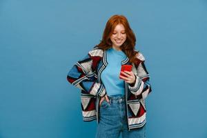 femme gingembre souriante en pull multicolore utilisant un téléphone portable photo