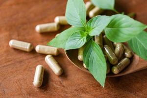 capsules à base de plantes d'herbes mode de vie sain - extrait de plantes médicinales de la nature médicament non toxique produit biologique sur cuillère en bois et feuille de basilic vert photo