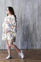 fille enceinte en robe sur fond de mur gris.