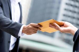 portrait en gros plan d'une main d'homme d'affaires recevant une enveloppe jaune du patron en arrière-plan de la ville urbaine photo