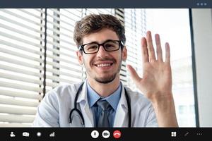 jeune homme médecin agitant la main saluant le patient en ligne par appel vidéo, concepts de service de consultation médicale à domicile photo