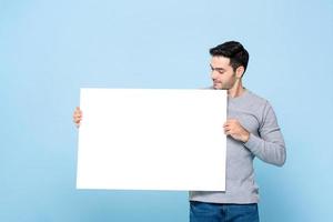 portrait d'un bel homme caucasien tenant et regardant une pancarte blanche sur fond bleu studio isolé photo