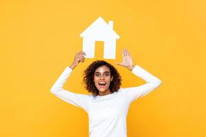 jeune femme souriante tenant un modèle de découpe de maison au-dessus sur fond jaune isolé photo