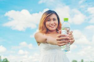 concept de mode de vie des femmes jeune jolie femme vêtue d'une robe blanche tenant une bouteille d'eau au smiley des prairies à l'appareil photo si frais et heureux.