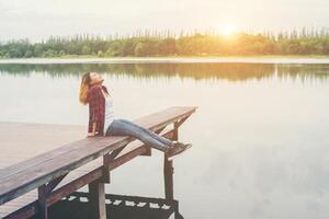 jeune femme hipster assise sur une jetée en bois, se relaxant la jambe allongée jusqu'au lac. photo