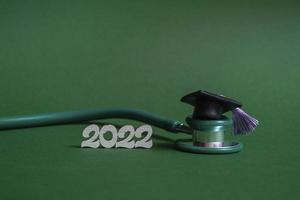 chapeau de graduation avec stéthoscope et numéros 2022 sur fond vert, gros plan avec espace de copie. concept d'éducation médicale. photo