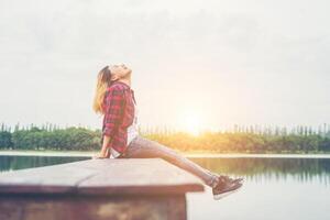 jeune femme hipster assise sur une jetée en bois, se relaxant la jambe allongée jusqu'au lac. photo