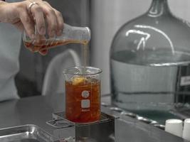 main de barista tenant un bécher en verre borosilicaté de laboratoire mélangeant une boisson de thé dans un cocktail de bécher de bar de chimie. photo