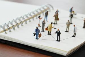 gros plan de personnes miniatures avec diagramme de réseau social sur un cahier ouvert sur un bureau en bois comme concept de médias sociaux photo