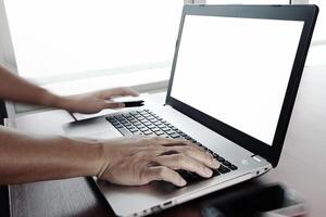 Gros plan de la main de l'homme d'affaires travaillant sur un ordinateur portable à écran blanc sur un bureau en bois comme concept photo