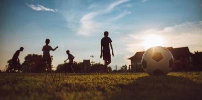 Sport d'action silhouette à l'extérieur d'enfants s'amusant à jouer au football football pour l'exercice dans la zone rurale de la communauté sous le ciel coucher de soleil crépusculaire