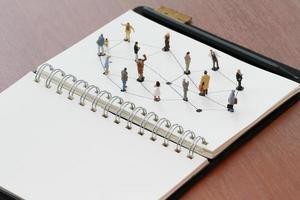 gros plan de personnes miniatures avec diagramme de réseau social sur un cahier ouvert sur un bureau en bois comme concept de médias sociaux photo